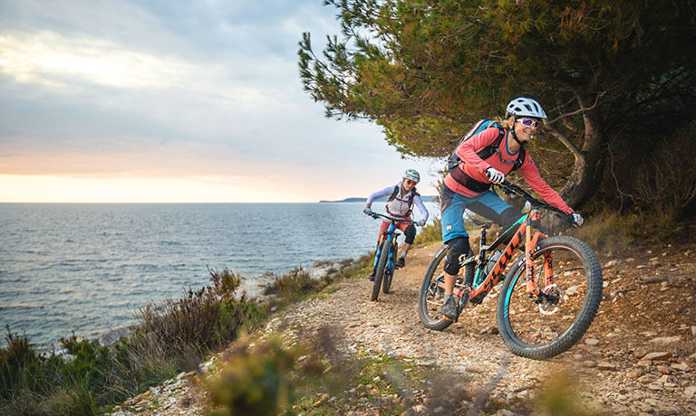 a couple of people riding bikes on a trail by the water