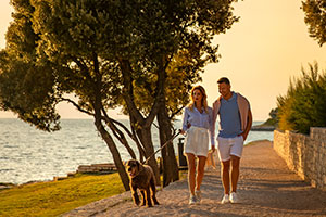 a man and woman walking a dog on a path by a body of water